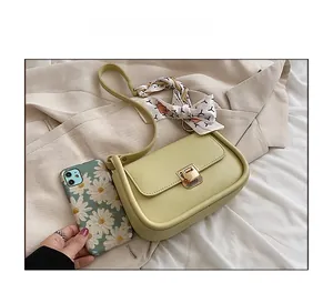 Close-up of light green crossbody bag with gold lock and decorative silk scarf accessory