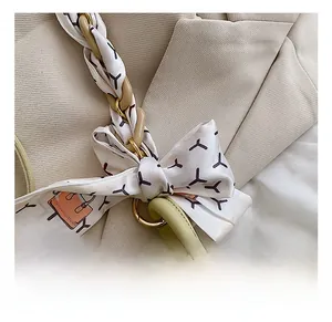 Detail of light green leather bag featuring silk scarf strap and golden chain hardware