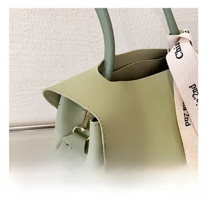 Detail of green leather handbag featuring golden metal hook and woven strap with ribbon