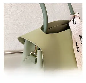 Detail of light green faux leather handbag with gold metal hardware and decorative silk scarf