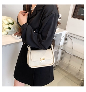 Detail of cream white leather crossbody bag with gold lock worn on shoulder in modern interior