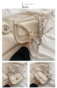 Detail of off-white leather crossbody bag with golden clasp and silk scarf accessory