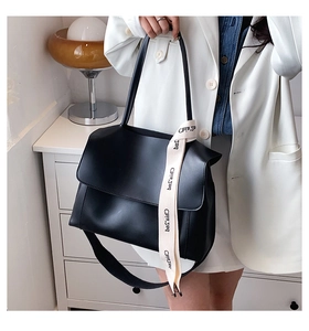 Close-up of black matte leather tote with beige decorative ribbon and flap closure