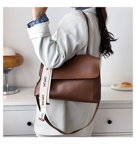 Brown leather shoulder bag detail with interchangeable thin strap and wide fabric strap