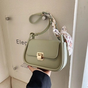 Sage green crossbody bag with silk scarf handle and gold square buckle on textured wall