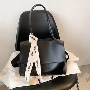 Large black leather tote bag with unique lettered strap on minimalist white shirt background