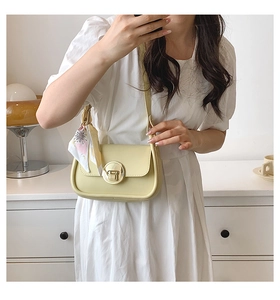 Close-up of pale yellow crossbody bag with gold lock and decorative silk scarf detail