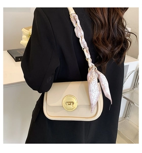 Detail of beige square crossbody bag featuring a golden circular lock and floral silk scarf