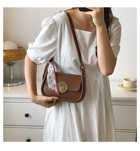 Detail view of brown leather shoulder bag with gold metal buckle and floral silk scarf