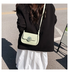 Detail of a light green leather crossbody bag with a round gold buckle on a model