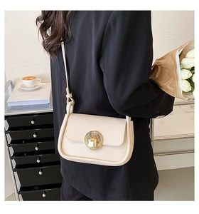 Chic cream crossbody bag with gold round buckle worn by a model in a stylish urban setting