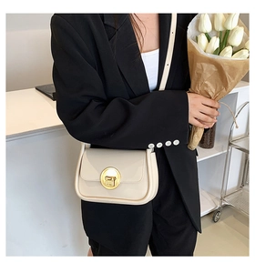 Detail of a creamy beige crossbody bag with gold round lock worn with black blazer