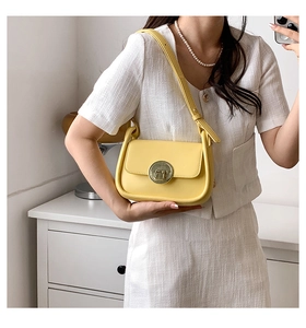 Detail of yellow shoulder bag featuring a large round gold buckle and flap closure