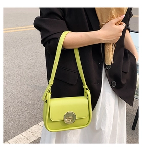Detail of bright green shoulder bag with golden round metal clasp on a leather surface