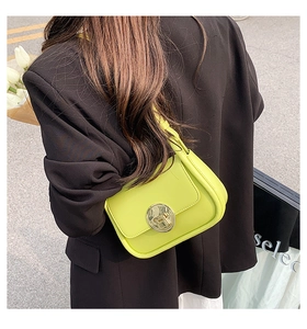 Close-up of lime green crossbody bag with gold metal clasp on a dark blazer outfit