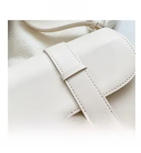 Detailed close-up of cream leather saddle bag showing strap stitching and matte finish