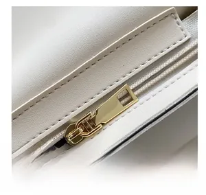 Detail showing smooth gold metal zipper and stitching on the cream leather handbag