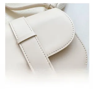 Detail view of precise stitching and matte leather texture on a beige saddle bag