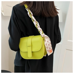 Lime green saddle bag with silk scarf chain strap worn by a model in a minimal setting