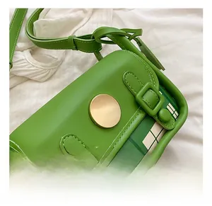 Close-up of green leather crossbody bag with golden metal buckle and white stitching details