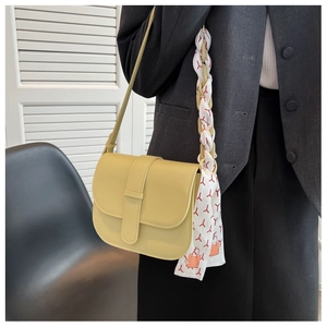Detail of a creamy yellow half-moon saddle bag featuring a stylish red floral silk scarf