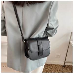 Detail of a black matte leather saddle bag worn by a model in a light blue suit