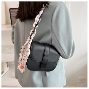 Detail of black PU leather saddle bag with decorative floral scarf on shoulder strap