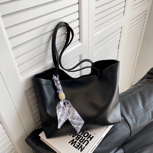 Grand sac cabas noir minimaliste en cuir avec foulard en soie et pendentif sur un livre