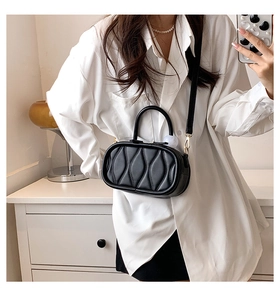Close-up of black crossbody bag with quilted wave texture worn over a white shirt