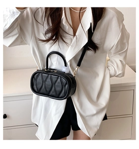 Model wearing a black quilted oval handbag with gold hardware and a slim shoulder strap