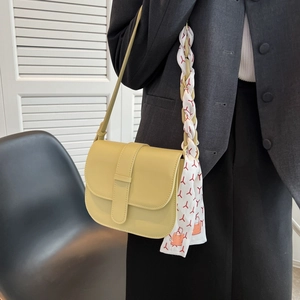 Pale green leather saddle bag with scarf handle worn by model in grey blazer