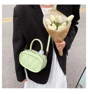 Detail of light green quilted handbag with wave pattern and soft blue fur ball charm