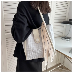 Detail of white textured tote bag with 'FASHION' ribbon and faux leather strap detail