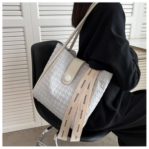 Detail of white pleated tote bag with faux leather straps and fashion pendant on a chair