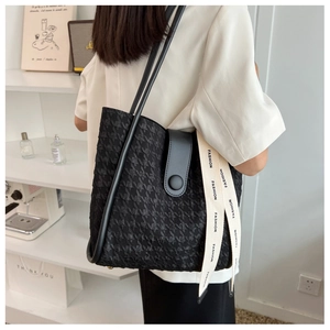 Side view of a black quilted tote bag featuring leather straps and a fashion woven ribbon