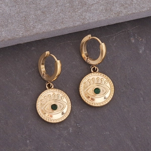 Detail van gouden oorringen met boze oog munten en groene edelstenen op natuursteen