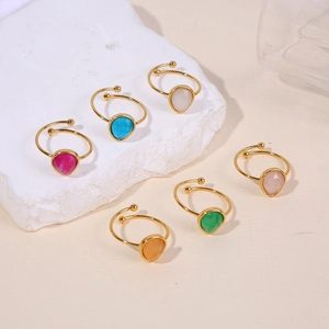 Group of six golden open rings with colorful teardrop stones on stone display
