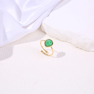 Macro shot of an adjustable gold ring featuring a faceted green gemstone on a stone texture