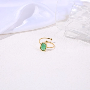 Close-up of a gold-plated ring with a square green natural stone on white sand