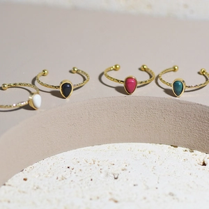 Set of four teardrop stone open rings in gold with colorful gemstones on a stone pedestal