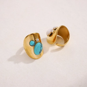 Close-up of vintage wide gold rings with turquoise and white stones on beige background