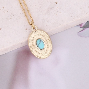 Vintage gold oval necklace with sunburst texture and turquoise stone on a stone surface