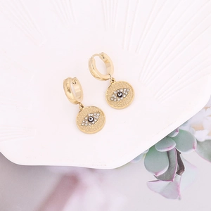 Détail des boucles d'oreilles œil porte-bonheur dorées avec strass sur plateau blanc