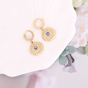 Gros plan de boucles d'oreilles œil porte-bonheur dorées sur un plateau coquillage