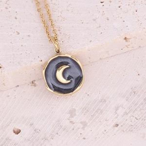 Golden round necklace with black inlay and crescent moon pendant on stone background