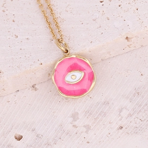 Macro shot of gold necklace with pink enamel evil eye pendant on textured stone