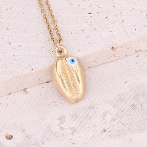 Detailed view of a gold shell pendant necklace with blue evil eye on stone surface