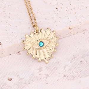 Close-up of gold heart necklace with evil eye motif on a textured stone background