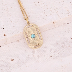 Macro detail of a golden rectangular pendant featuring sunburst engraving and blue gemstone