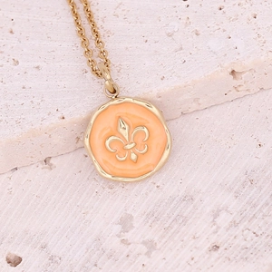 Macro detail of gold necklace featuring an orange enamel pendant with a fleur-de-lis emblem